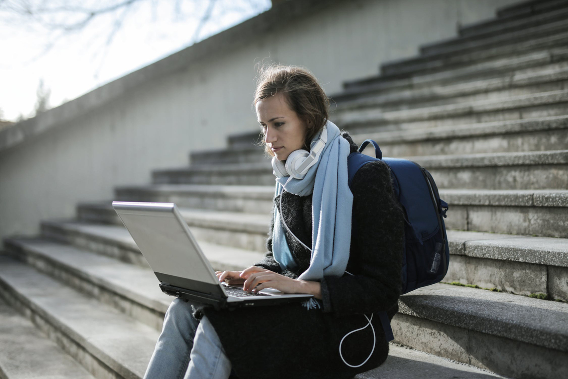 Studentin auf einer Treppe sitzend mit Laptopr echerchiert Studienfinanzierung